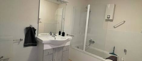 Un baño moderno con lavamanos, espejo y bañera blancos.