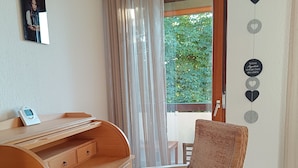 Ein Zimmer mit einem Holztisch, einem Korbstuhl, einem Fenster mit Vorhängen und einer Wanddekoration.