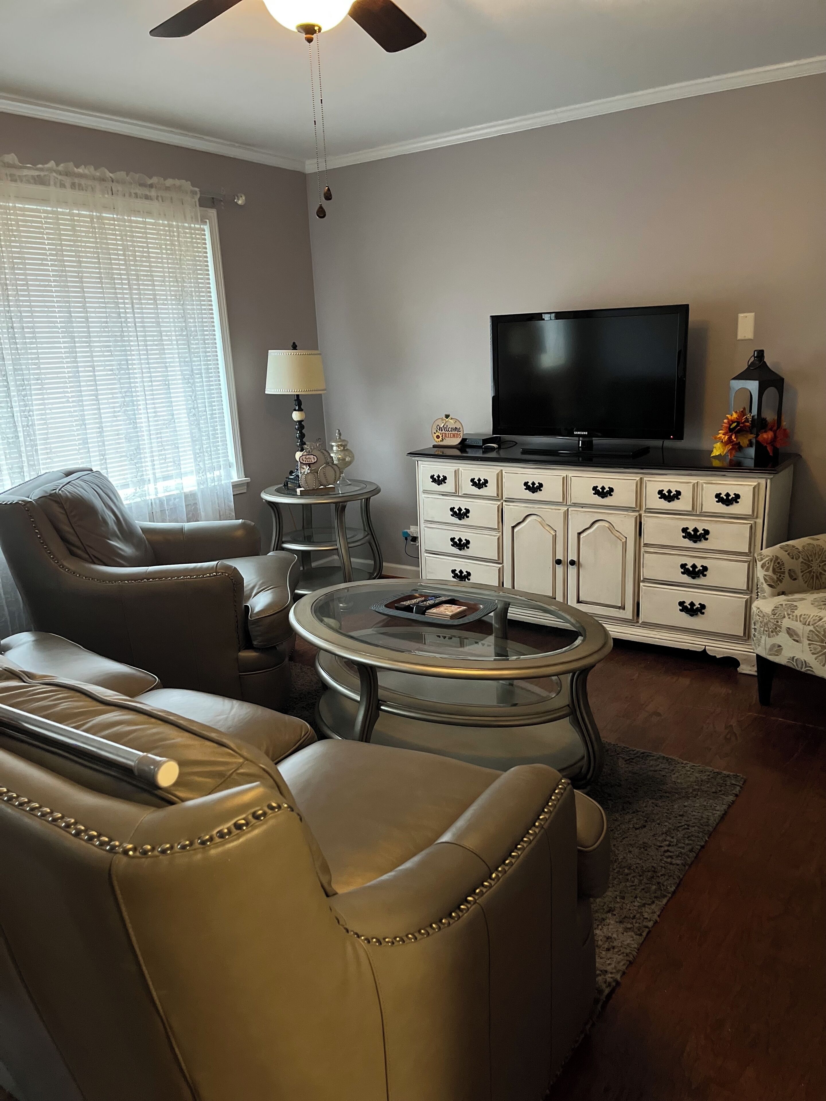 A living room with a leather sofa, a glass coffee table, a TV on a cabinet, and a lamp.