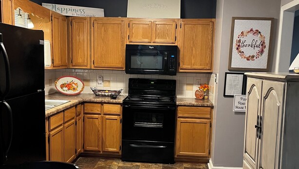 A kitchen with wooden cabinets, a black stove, a microwave, and a refrigerator.