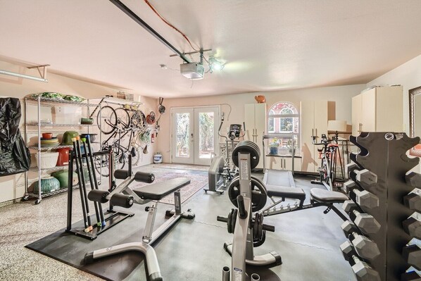 A home gym with various exercise equipment, a window with a view, and a door leading outside.