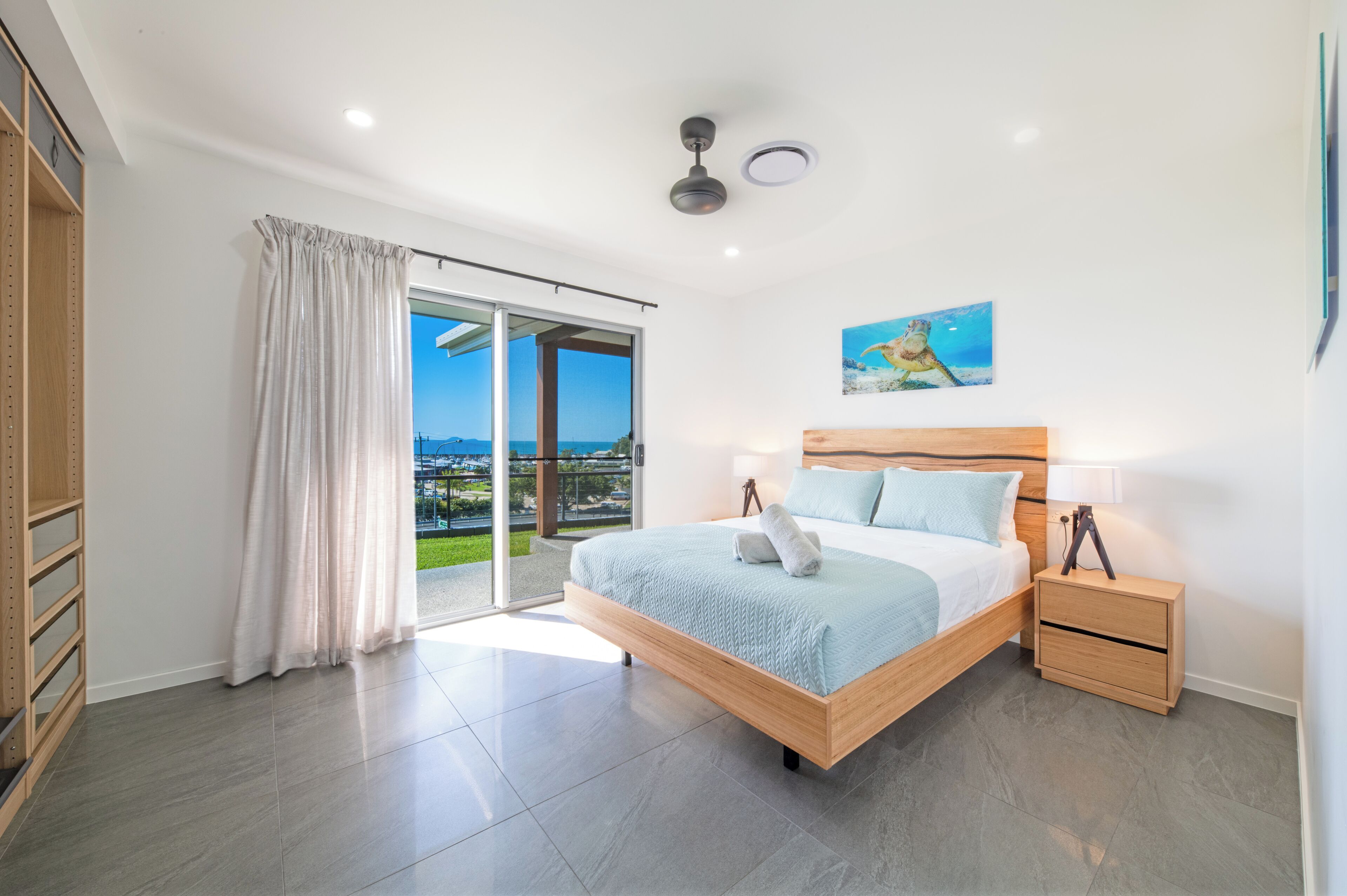 A bedroom with a large bed, a nightstand, a window with curtains, and a view of the outside.