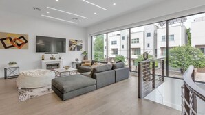 Una sala de estar moderna con un sofá seccional gris, un sillón tipo bean bag blanco, un televisor de pantalla plana y obras de arte en las paredes.
