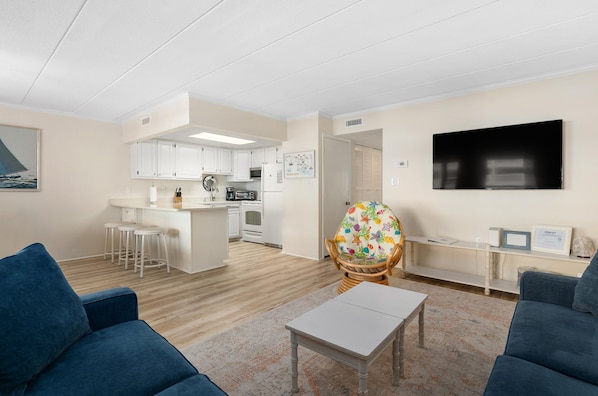 A modern living room with a sofa, a coffee table, and a dining area with a kitchen in the background.