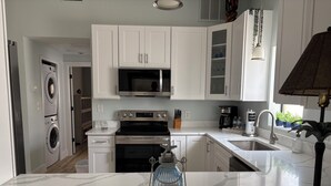 Una cocina moderna con armarios blancos, horno empotrado, microondas y lavadora.