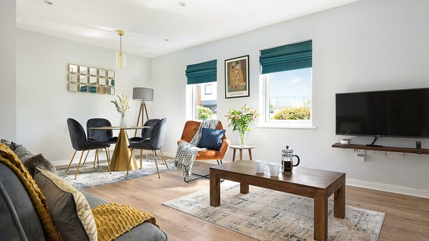 Ein modernes Wohnzimmer mit Sofa, Couchtisch und Fernseher. Es gibt eine Essecke mit Stühlen und einem Tisch, und eine Pflanze auf einem Beistelltisch.