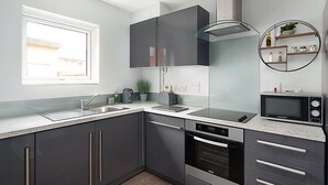 Eine moderne Küche mit grauen Schränken, einer Edelstahlspüle, einem Backofen und einer Mikrowelle.