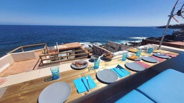 A dining area on a boat with a view of the sea, featuring a wooden table with plates, glasses, and napkins. - House above the sea. Impressive. (La Puente)