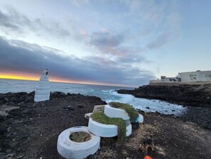 A coastal scene with a rocky shoreline, a small structure with tires stacked as seating, and a building in the background. - House above the sea. Impressive. (La Puente)