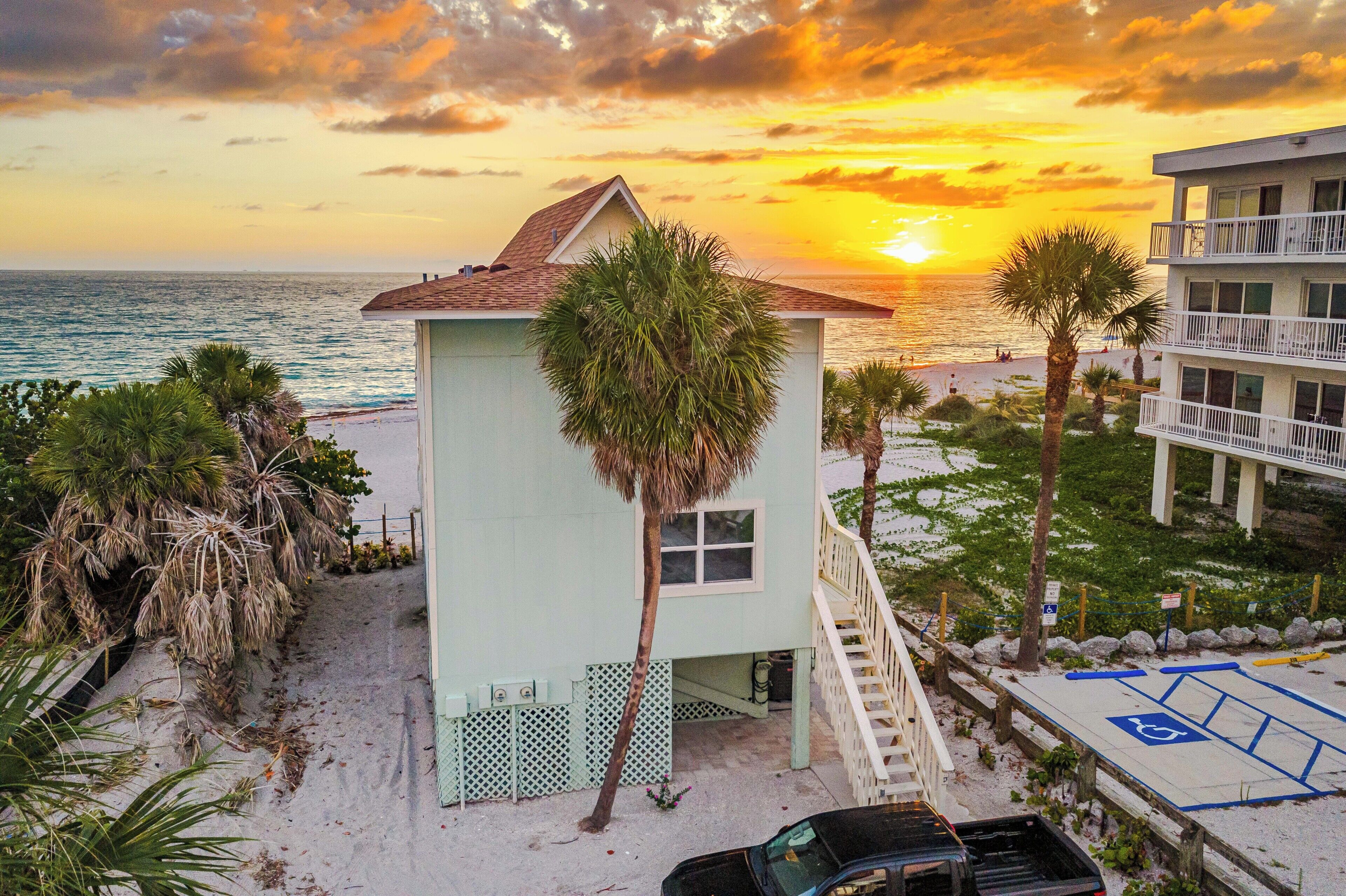 Un immeuble situé en bord de mer, doté d’un petit balcon, d’un escalier et offrant une vue sur l’océan au coucher du soleil.