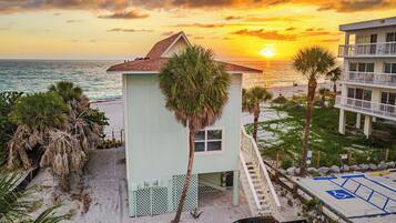 Un immeuble situé en bord de mer, doté d’un petit balcon, d’un escalier et offrant une vue sur l’océan au coucher du soleil.