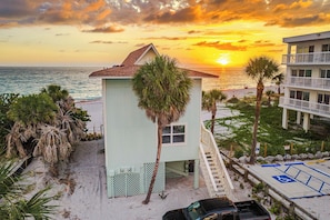 A beachfront building with a small porch, a staircase, and a view of the ocean at sunset.