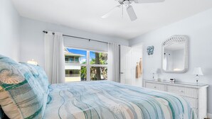 A bedroom with a bed, a ceiling fan, a window with curtains, a white dresser, and a mirror.
