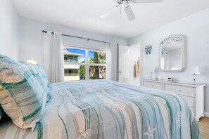 A bedroom with a bed, a ceiling fan, a window with curtains, a white dresser, and a mirror.