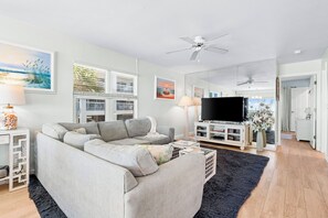 A modern living room with a sectional sofa, a flat-screen TV, and a ceiling fan.