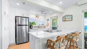 A modern kitchen with a stainless steel refrigerator, white cabinetry, and a large island with bar stools.