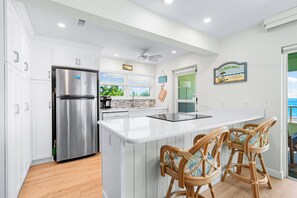 A modern kitchen with a stainless steel refrigerator, white cabinetry, and a large island with bar stools.