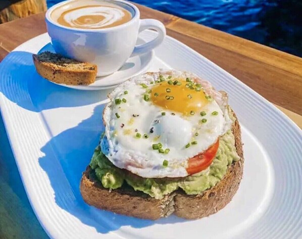 A breakfast plate with an egg, avocado, and tomato on toast, accompanied by a cup of coffee. - Oceanfront, Directly On The Beach Condo w/Amazing  Views of the Gulf! (Englewood)