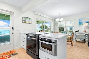 Een moderne keuken met een ingebouwde oven en een aparte magnetron, een eethoek met uitzicht op het strand, en een gezellig zitje met een stoel en een tafeltje.