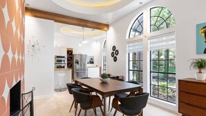 A modern kitchen with a dining area, featuring a large wooden table, black chairs, and a view of the outdoors through large windows. - Unique Mid Century Modern in The Woodlands (Spring)