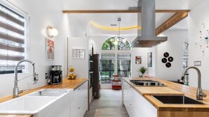 A modern kitchen with white cabinetry, wooden countertops, and stainless steel appliances. There is a large window with a view of greenery outside. - Unique Mid Century Modern in The Woodlands (Spring)