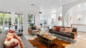 A modern living room with a sofa, armchair, and coffee table, large windows, and a view of the outdoors. - Unique Mid Century Modern in The Woodlands (Spring)