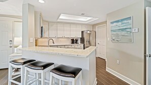 Una cocina moderna con armarios blancos, una isla central con taburetes altos, un refrigerador y una cafetera.