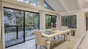 A dining area with a glass-top table, cushioned chairs, and large windows offering views of a residential area. - 7 Bald Eagle-3 Row Ocean (75 yards) to the Beach &  40 ft x 10 ft Pool (Hilton Head Island)