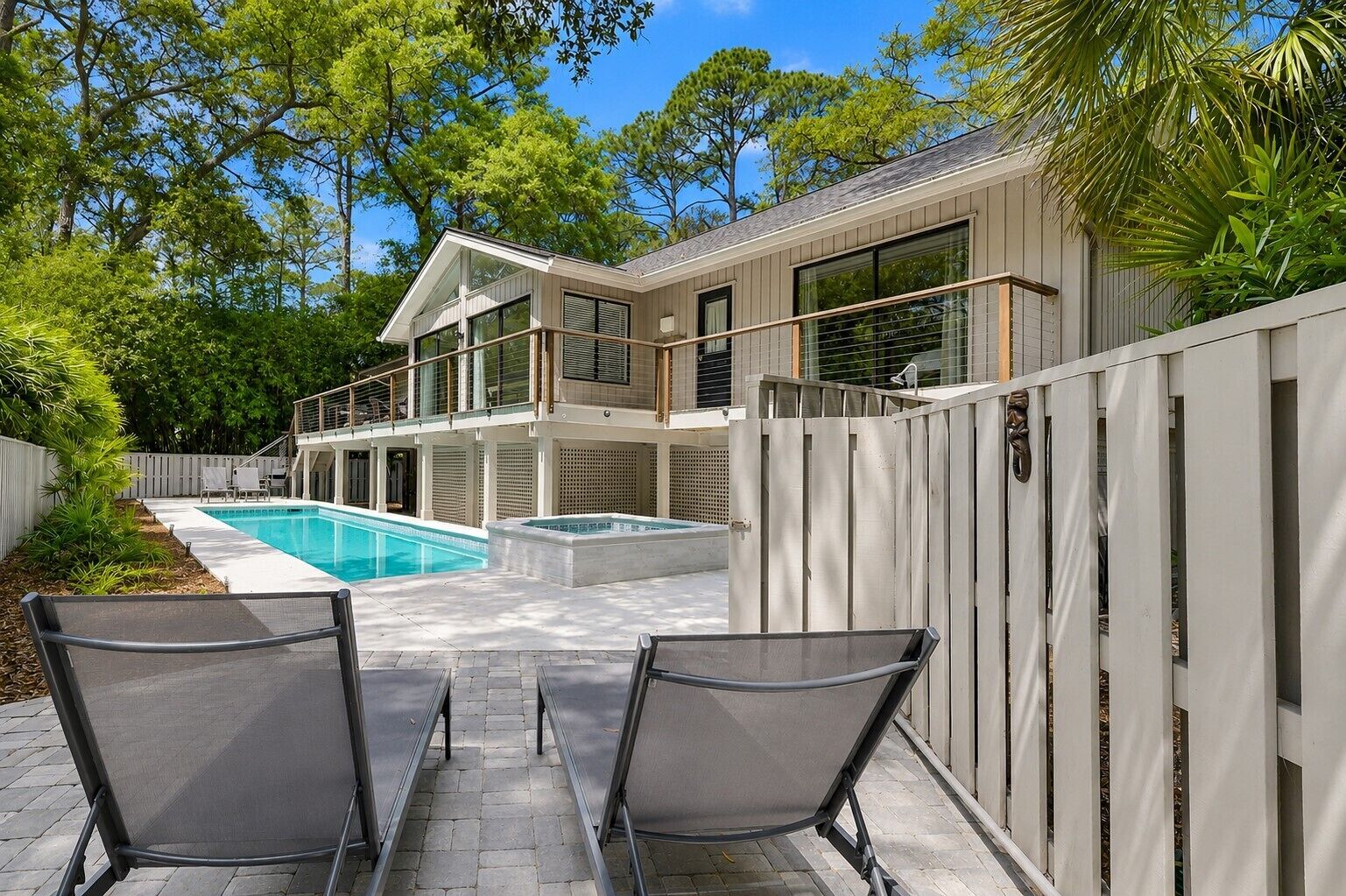 A modern house with a swimming pool, two lounge chairs, and a covered patio area.