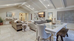 A spacious living room with a high ceiling, a dining area with a glass-top table, and a large TV mounted on the wall. - 7 Bald Eagle-3 Row Ocean (75 yards) to the Beach &  40 ft x 10 ft Pool (Hilton Head Island)