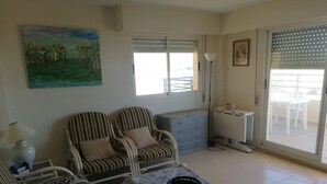 A living room with two striped armchairs, a patterned sofa, a coffee table with a black bowl, a radiator, and a balcony with a table and chairs. - El pilar 6º Solo familias! (Xeraco Playa)