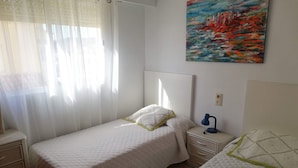 A bedroom with two beds, a nightstand with a lamp, a dresser, and a painting on the wall. - El pilar 6º Solo familias! (Xeraco Playa)