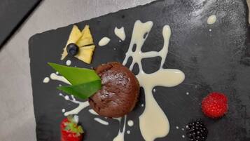 A dessert on a black slate plate with white sauce, a strawberry, a raspberry, a blackberry, a blueberry, and a green leaf.