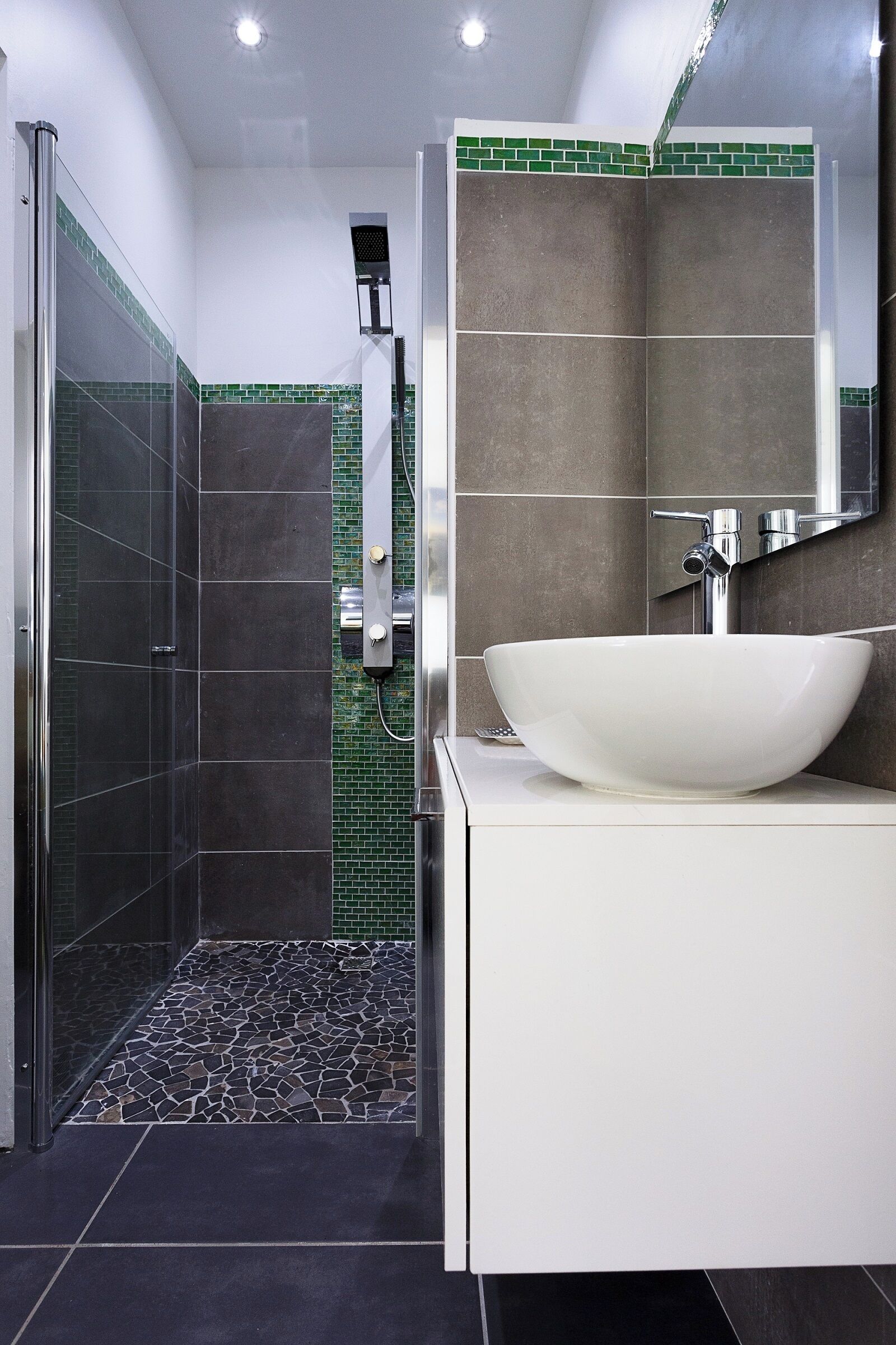 Une salle de bain moderne avec un grand lavabo sur pied blanc, une douche à parois de verre et un sol carrelé.