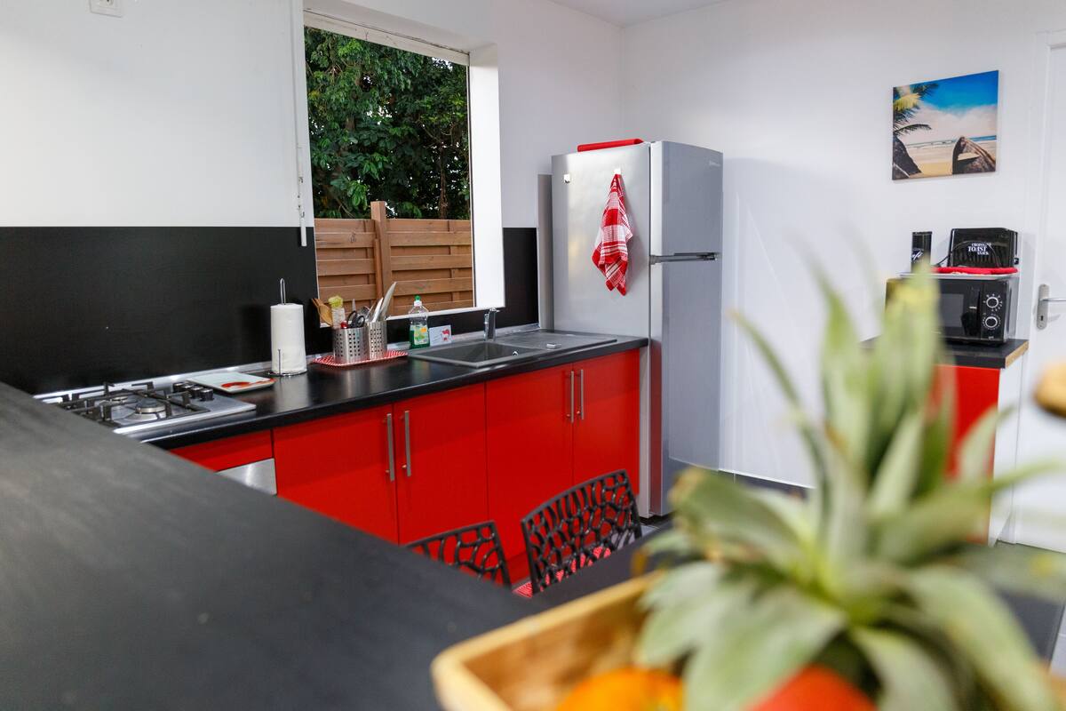 A modern kitchen with red cabinets, a stainless steel refrigerator, and a window overlooking greenery.
