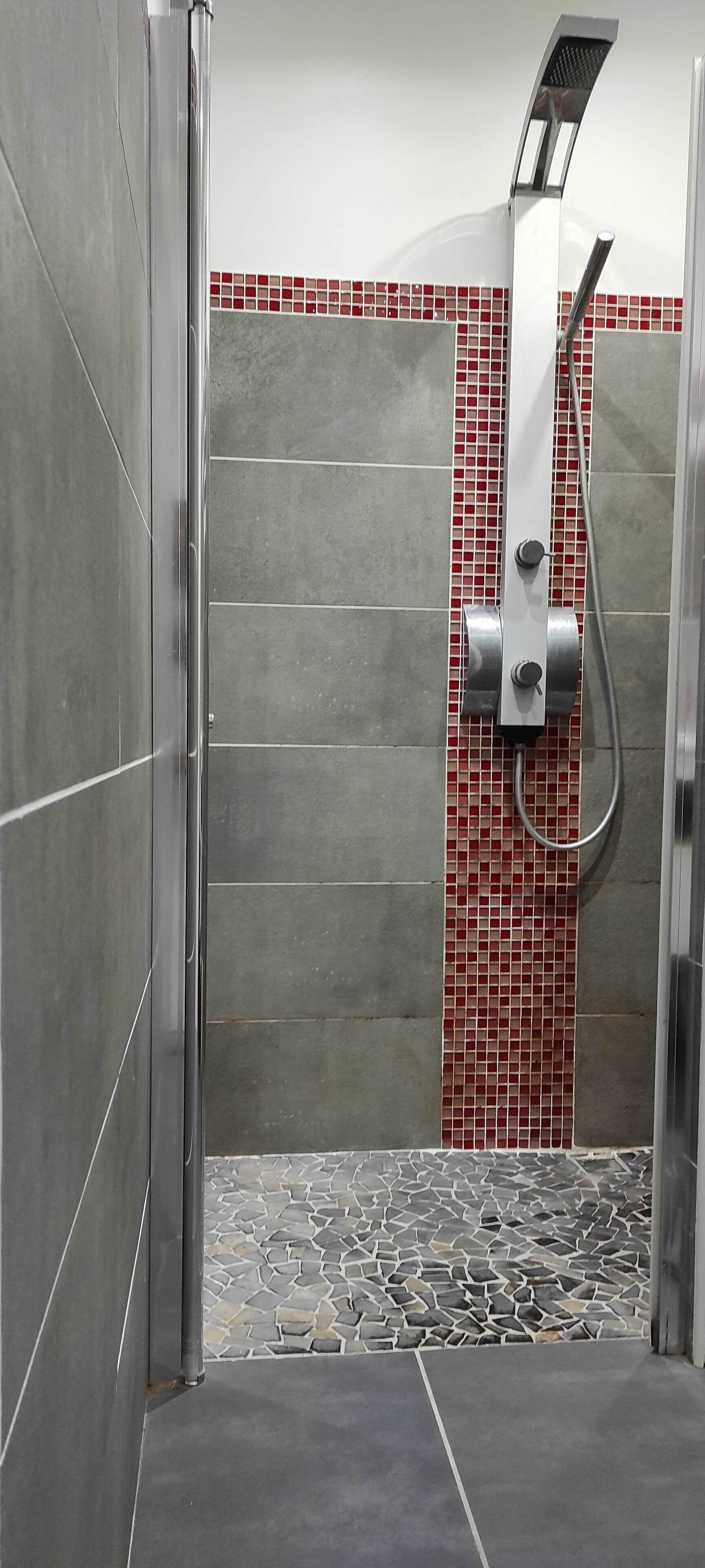 Un área de ducha con piso de baldosas, un cabezal de ducha y una pared con azulejos rojos y grises.