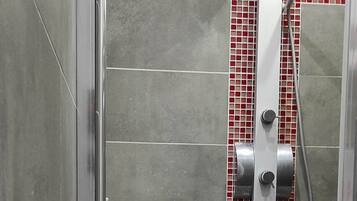 Un área de ducha con piso de baldosas, un cabezal de ducha y una pared con azulejos rojos y grises.