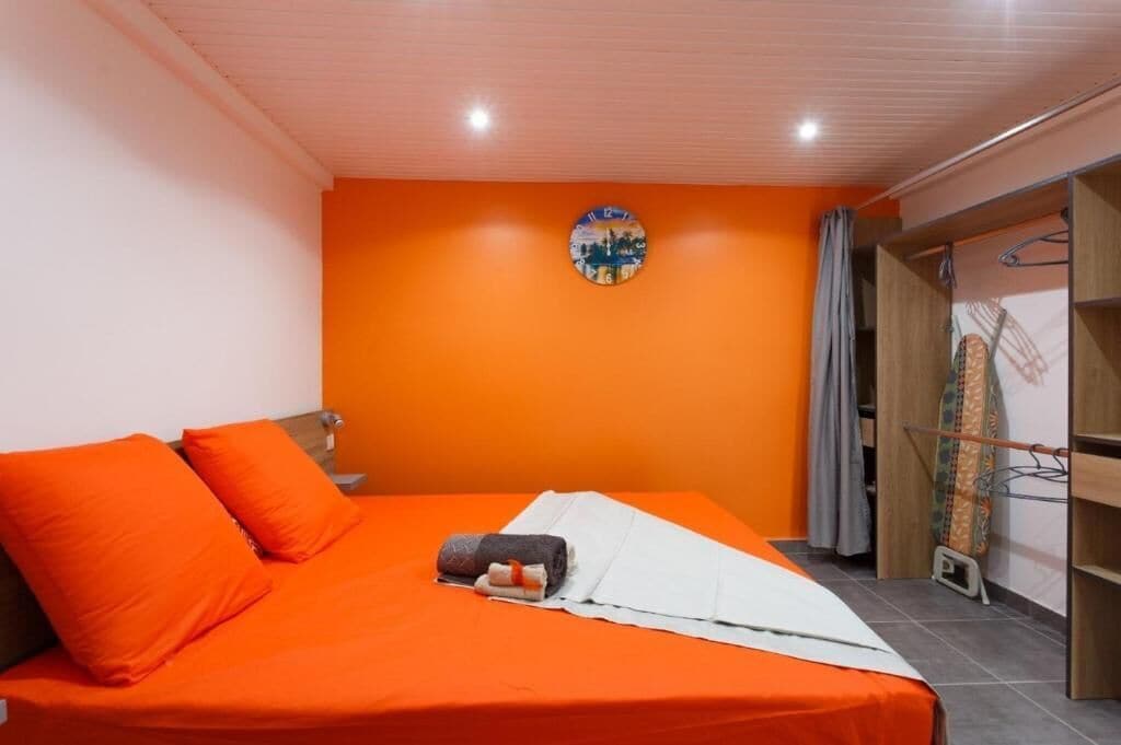 Une pièce avec un lit, des murs orange, une horloge et une armoire.