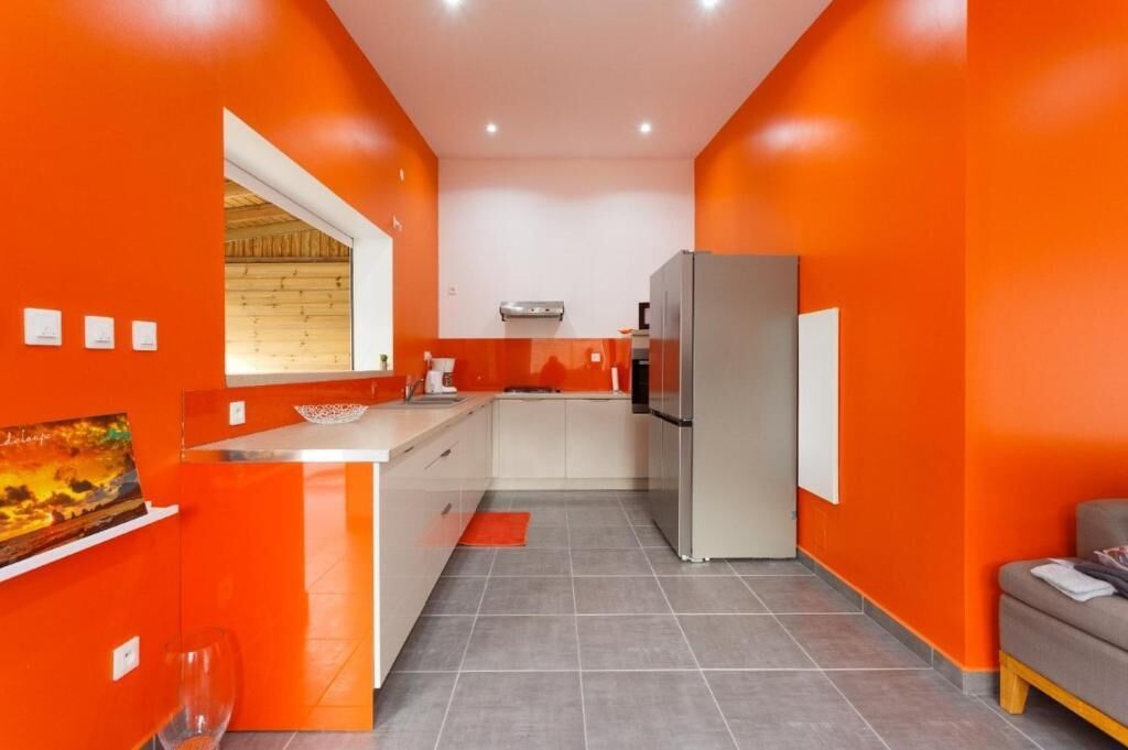 A compact kitchen with orange walls, a refrigerator, and a window.