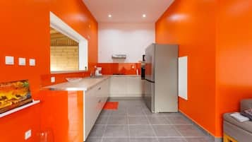 A compact kitchen with orange walls, a refrigerator, and a window.