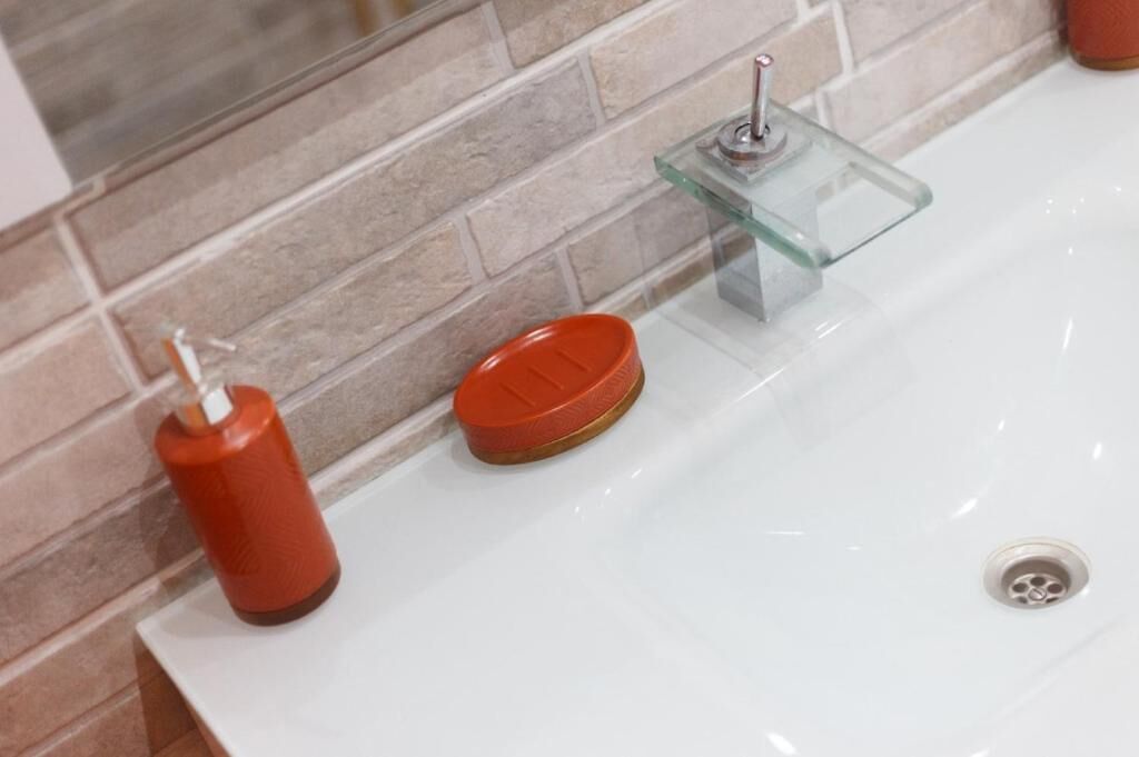 Un lavamanos con un posavasos de vidrio y un dispensador de jabón rojo.
