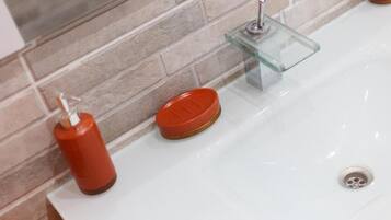 Un lavamanos con un posavasos de vidrio y un dispensador de jabón rojo.