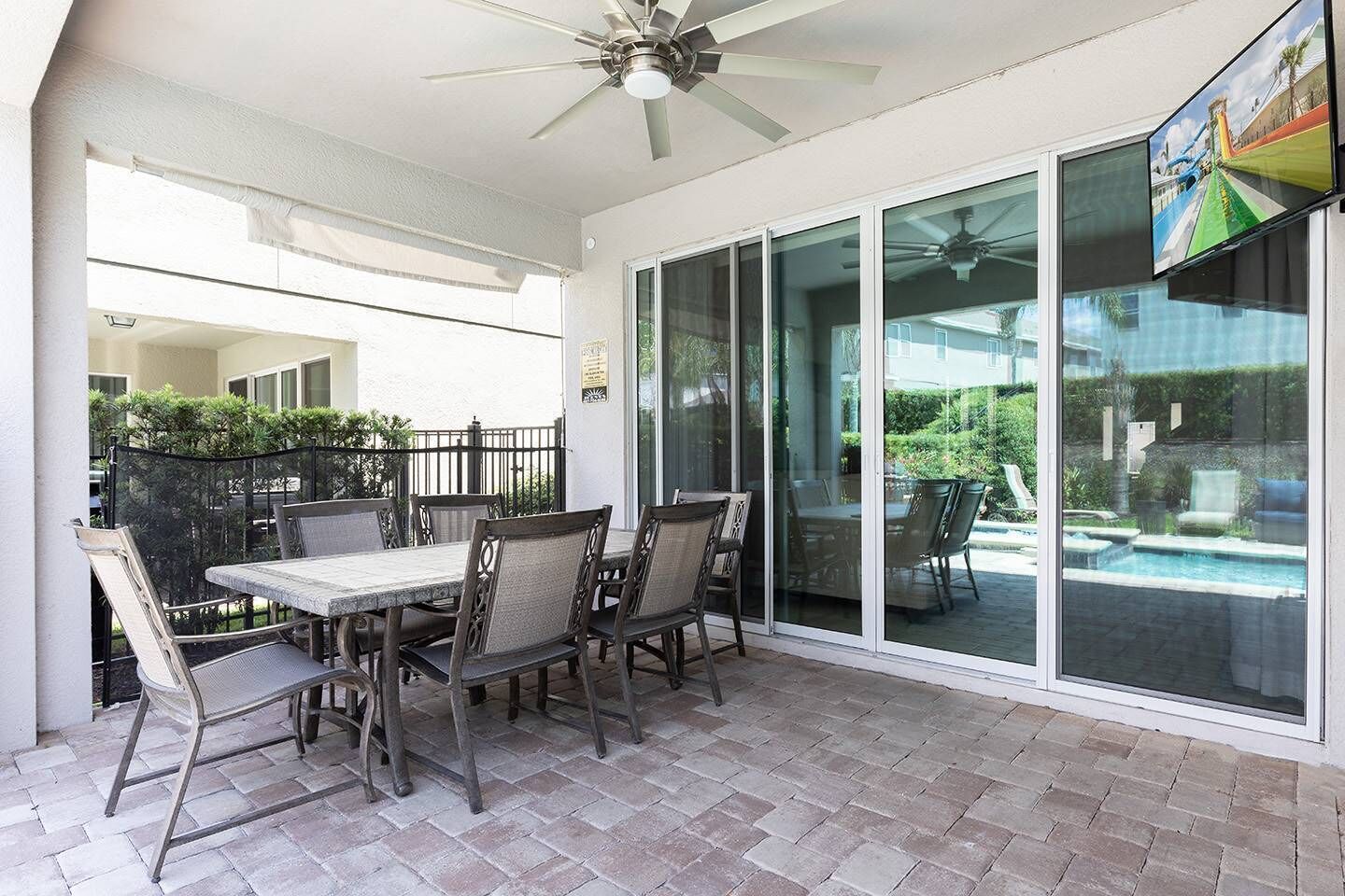 A covered patio with a table and chairs, a ceiling fan, and a view of a swimming pool through glass doors.