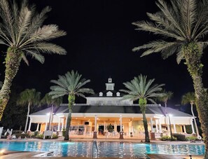 A hotel with a pool, palm trees, and a lit-up building at night.