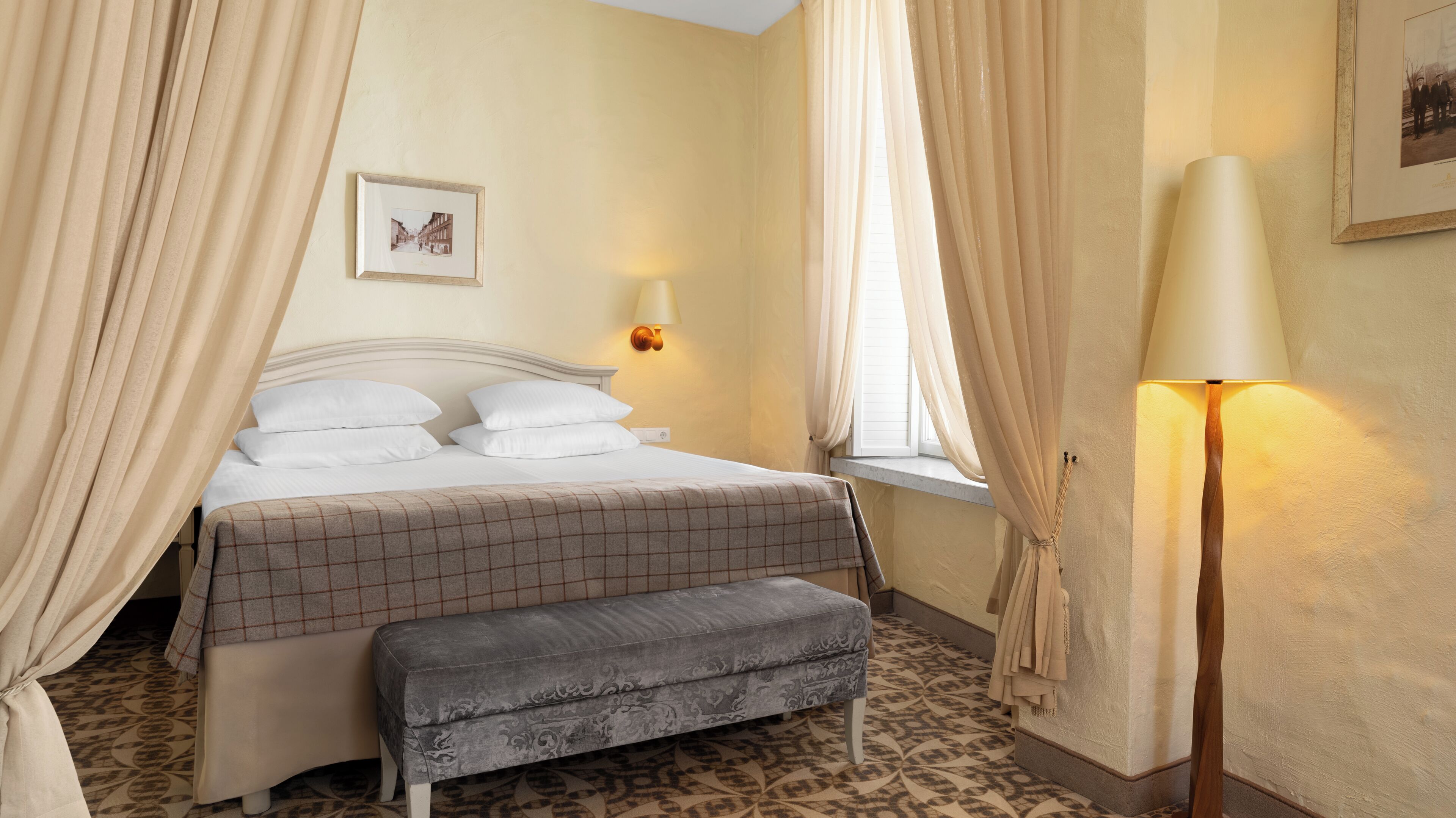 Un dormitorio ordenado con una cama, una lámpara de noche y un cuadro en la pared.