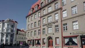 Ein mehrstöckiges Gebäude mit rotem Dach, einer Schrifttafel mit der Aufschrift 'SAVOY BOUTIQUE Hotel' und einer roten Markise über dem Eingang.