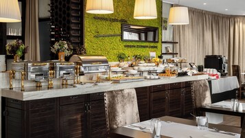 Una barra de buffet con diversos alimentos, una máquina de café y una torre de vinos.