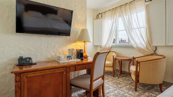 Habitació d'hotel amb escriptori de fusta, una cadira, televisió, làmpada, finestra amb cortines i terra amb disseny.