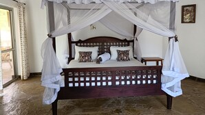 Uma cama de dossel com estrutura de madeira, roupa de cama branca e almofadas estampadas.