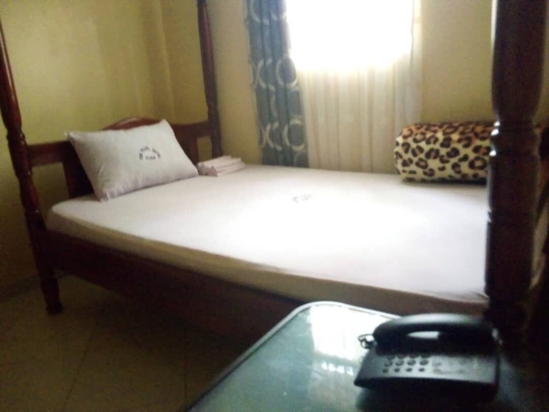 A hotel room with a single bed, a bedside table with a telephone, and a window with curtains.